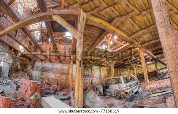 Panorama\
of a messy, wrecked, abandoned barn interior with trash piling\
inside and sun shining through the damaged\
roof