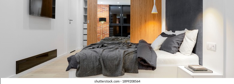 Panorama of modern and comfortable, loft style bedroom with big bed, tv and wardrobe with wooden and mirror door