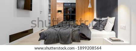 Panorama of modern and comfortable, loft style bedroom with big bed, tv and wardrobe with wooden and mirror door