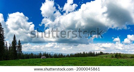 Panorama of a mountain meadow, blue sky and clouds. View from the mountain. Travel and vacation in the mountains.