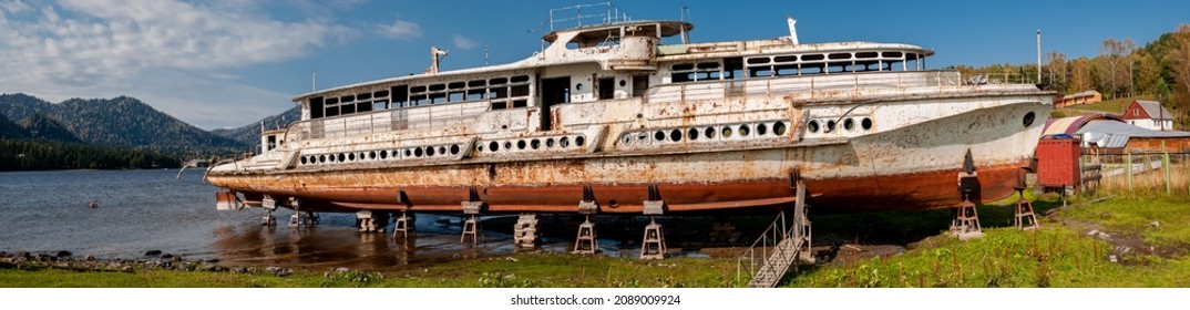 Panorama of an old rusty abandoned iron ship near the lake. The Pioneer ship on the shores of Lake Teletskoye. Mountain Altai - Powered by Shutterstock