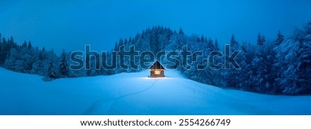 Panorama of picturesque winter landscape with glowing wooden cabin in snowy forest. Cozy house in Carpathian mountains. Christmas holiday concept