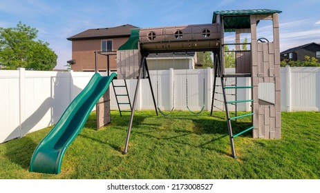 Panorama Playground At The Backyard With Lawn And Vinyl Fence At Utah. Playground Set With Swing And Slide On Top Of A Green Lawn And A View Of The Neighborhood And Skyline.