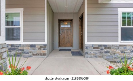Panorama Porch of a house with potted flowers and two wooden front doors. Exterior of a house with gray vinyl wood and stone veneer sidings. - Shutterstock ID 2192806089