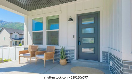 Panorama Porch with two woven armchairs and snake plant on a woven pot. Entrance exterior with black front door with glass panels and lockbox near the windows and a view of the neighborhood - Shutterstock ID 2192806077