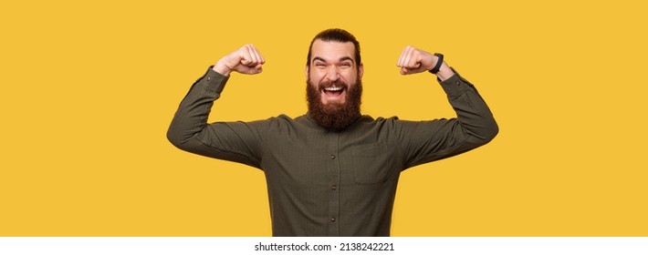 Panorama portrait of a bearded ecstatic man with arms in power gesture. Studio shot over yellow background.