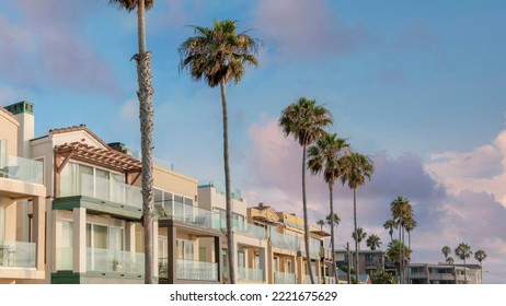Panorama Puffy clouds at sunset Row of multi-storey houses with attached garage at La Jolla, California. Houses with glass railings at the balconies and columnar palm trees at the front near the road.