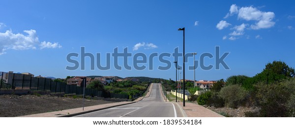 Panorama\
of road goes into the distance against a blue sky with clouds. On\
the sides trees and a small village. Copy\
space