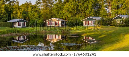Panorama with row of colorful wooden vacation home reflected in a pond at recreation park in the middle of nature in the Netherlands