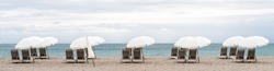 Panorama Of A Row Of Empty Brown Chairs And White Umbrellas Set Up On A Beach In The Early Morning,