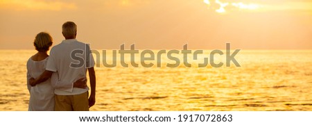 Panorama senior man and woman couple embracing at sunset or sunrise on a deserted tropical beach panoramic web banner, s3niorlife