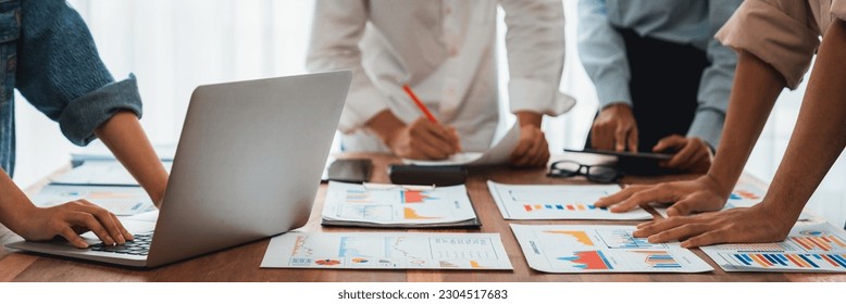 Panorama shot analyst team utilizing BI Fintech to analyze financial report with laptop. Businesspeople analyzing BI power dashboard displayed on laptop screen for business insight. Scrutinize