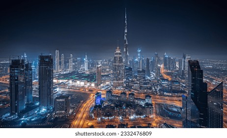 Panorama showing aerial view of tallest towers in Dubai Downtown skyline and highway night panorama. Financial district and business area in smart urban city. Skyscraper and high-rise buildings
