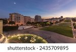 Panorama showing lawn at Alameda Dom Afonso Henriques with colorful buildings and illuminated Luminous Fountain aerial day to night transition from above after sunset in Lisbon, Portugal