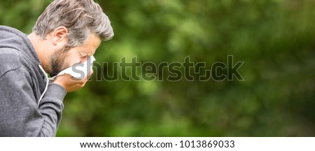 Panorama of sick or allergic man sneezing with tissue