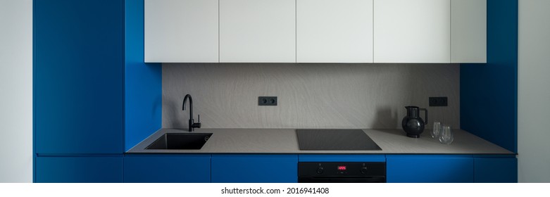 Panorama Of Simple, Modern And Small Kitchen With Blue And White Cupboards And Gray Countertop And Backsplash And Black Sink