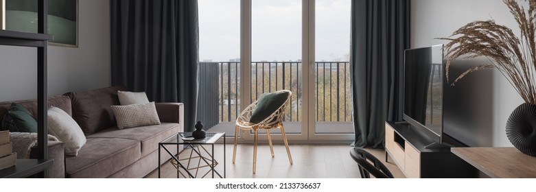 Panorama of small and elegant living room with cozy couch, modern furniture, tv and window doors to balcony