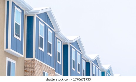 Panorama Snowy gable roofs at the facade of townhome with brick wall and vertical siding