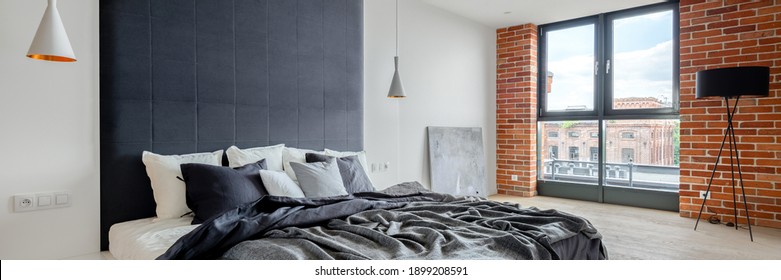 Panorama Of Spacious And Elegant Bedroom With Industrial Style Wall With Exposed Red Brick, Big Comfortable Bed With Upholstered Wall And Big Window