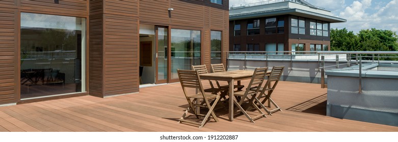 Panorama of spacious wooden terrace with simple wooden furniture in modern building, exterior view