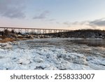 Panorama of the St. Lawrence river ice-covered coast, houses on Doré Street and the 1908 railway trestle bridge in the background seen during a winter dawn, Quebec City, Quebec, Canada