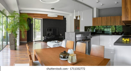 Panorama Of Stylish Apartment With Elegant Kitchen And Dining Area Open To Living Room Tv On Black Brick Wall