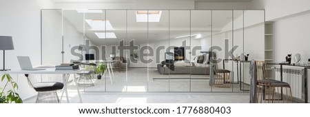 Panorama of stylish attic bedroom with gray bed, desk, ceiling windows and white walls and large wardrobe with mirror doors