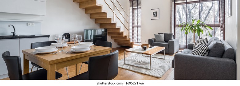 Panorama Of Stylish Two-floor Apartment With Kitchen And Dining Area Open To Living Room And Wooden Stairs To Higher Floor