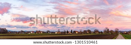 Panorama, sunset over fields and Austrian village with dramatic sky and colorful clouds