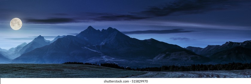 панорама Татр в дымке за лесом и сельским полем ночью в полнолунном свете
