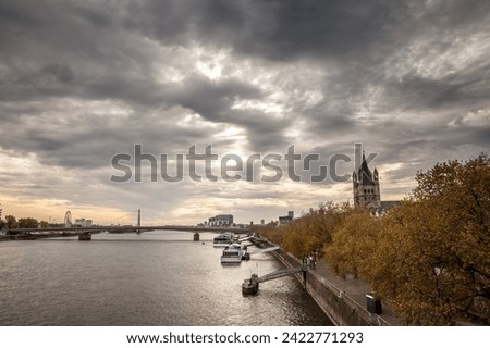 Panorama of trankgassenwerft promenade on the rhine river in Cologne, Germany, with cruise ships and boats anchored waiting for tourists at dusk in autumn. The Church of Gross St martin is visible.