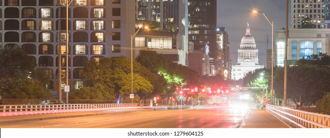 Panorama View Downtown Austin At Night With Traffic Light Trail Lead To Texas State Capitol Building. View From Pedestrian Sidewalk On Bridge Across Colorado River