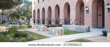 Panorama view multi-level brick structure college campus features arched ground-level openings and rectangular upper windows. Gravel beds, concrete benches and tree shadows blend in Waco, Texas. USA