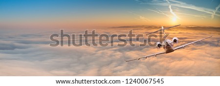 Panorama view of private jet plane flying above dramatic clouds during sunset.