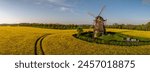 Panorama view of rapeseed field with three-story earth-hollander windmill. Banner from bright yellow rapeseed field with an old windmill.