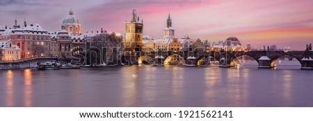 
panorama  view of snowy charles bridge at sunset in winter and pink colored sky with light in prague in czech republic