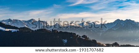 Panorama view of the snowy mountains between Switzerland, Liechtenstein and Austria. in foreground Austrian Alp with meadows and huts in the middle of the woods and in Background mountain range peaks