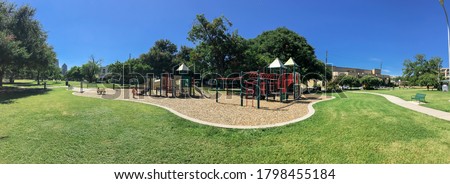 Panorama view urban playground at public park surrounded by large trees and skylines background in downtown Dallas, Texas, USA. Empty recreation place in hot summer day with sunny clear blue sky
