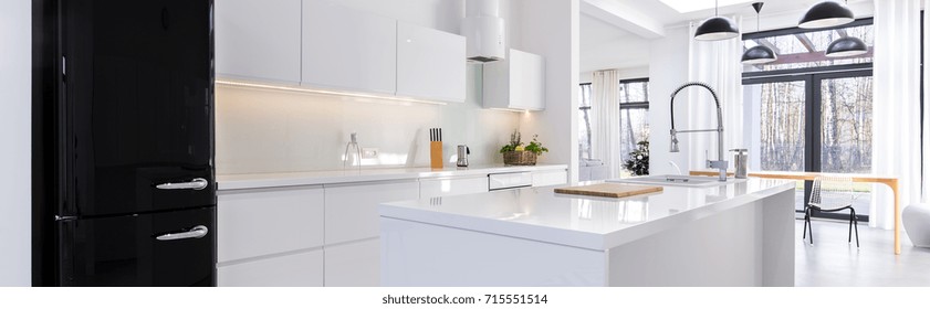 Panorama of white open kitchen with black fridge and built-in modern cabinets