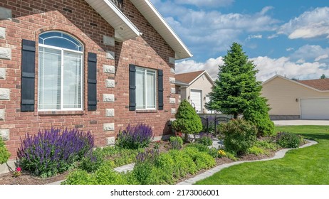 Panorama White puffy clouds Facade of a house with front yard garden and concrete walkway. House exterior with red bricks and decorative windows with black fake shutters and a view of a lawn