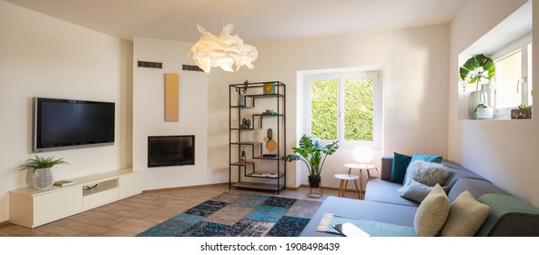 Panorama of wide modern living room with design sofa and large pillows above. Design library and small fireplace. Nobody inside