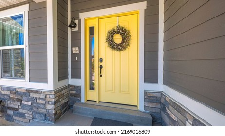 Panorama Yellow front door with wreath and sidelight at the entrance of a house in Utah. Home exterior with gray wood vinyl and stone veneer sidings and a porch with wall lamp near the window. - Shutterstock ID 2169016809