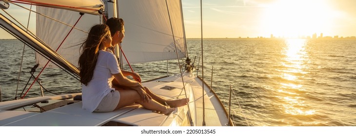 Panorama of young Hispanic couple at leisure sailing the ocean relaxing on luxury yacht watching the sunset on the horizon