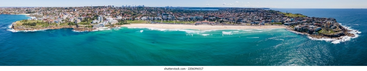 Panoramic Aerial Drone View Of Iconic Bondi Beach In Sydney, Australia Looking West Toward Sydney City In The Background On A Sunny Day During Spring 2022  