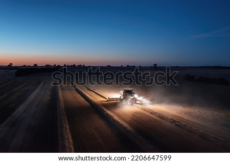 Panoramic aerial landscape view of working combine harvester at night with lights illuminating the field