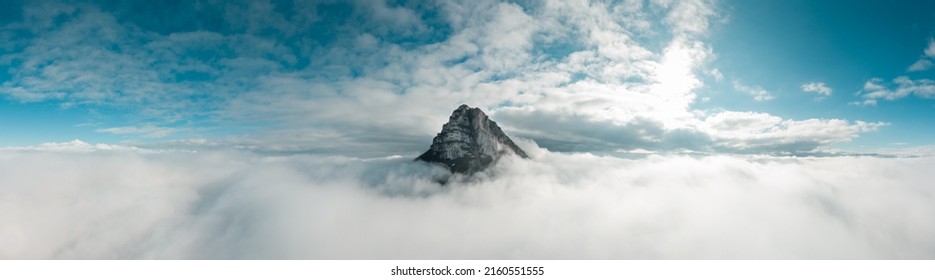 Panoramic aerial photograph taken with a drone. The peak of Beriáin, in the Andía mountain range, rises among the white clouds. In the background a deep blue sky and the sun rising through the clouds. - Powered by Shutterstock