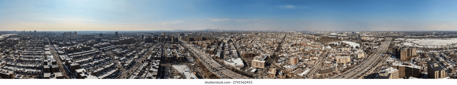 Panoramic aerial view capturing forest hills, queens, with snow dusted buildings, busy highways, and residential streets under a clear winter sky, extending across the new york city landscape