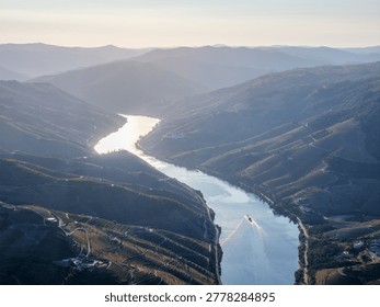 Panoramic aerial view of the Douro River and layered vineyard hills in Douro Valley, Portugal, with a tourist boat on the water.