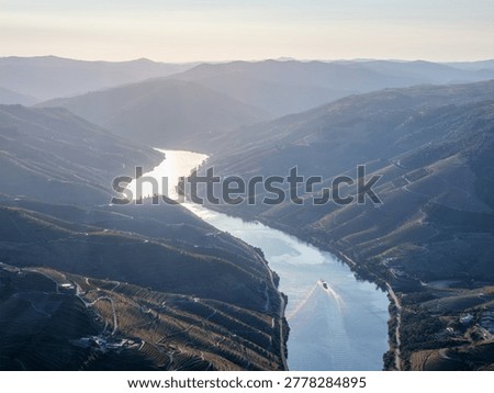 Panoramic aerial view of the Douro River and layered vineyard hills in Douro Valley, Portugal, with a tourist boat on the water.