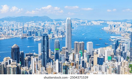 A panoramic aerial view of Hong Kong, showcasing its dense skyline with towering skyscrapers, Victoria Harbour, and lush green mountains in the background. - Powered by Shutterstock